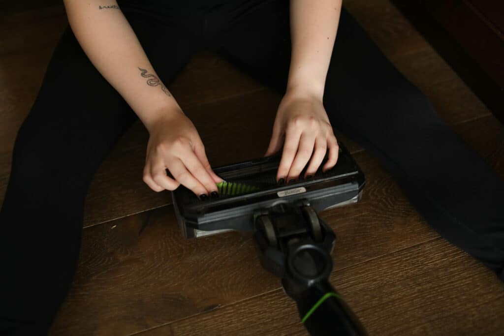 Go_Clean-Sept-2022-128 - House Work Person cleaning a vacuum brush attachment on a hardwood floor.
