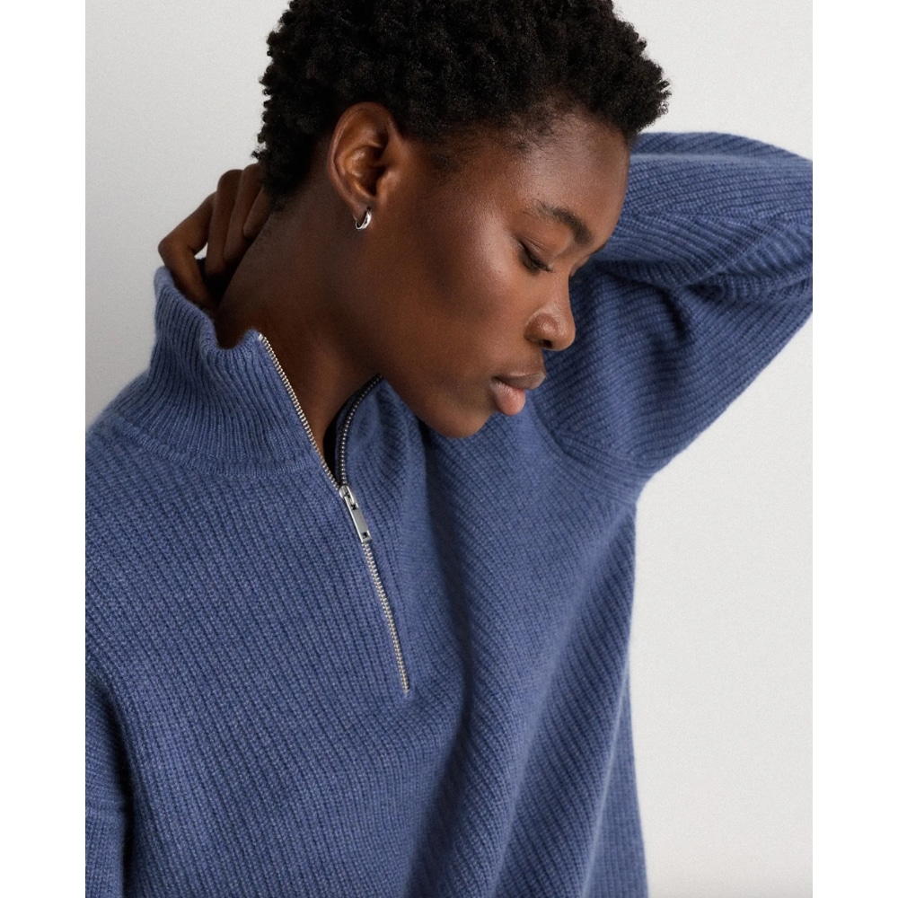 Side profile of a person wearing a blue knit pullover with a half-zip, head tilted downward and one hand at the back of the neck.