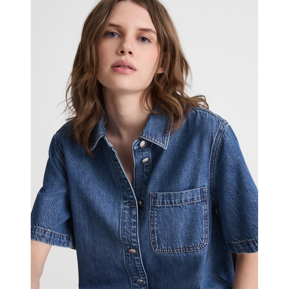 Woman wearing a blue denim button-up shirt with a chest pocket against a light background.