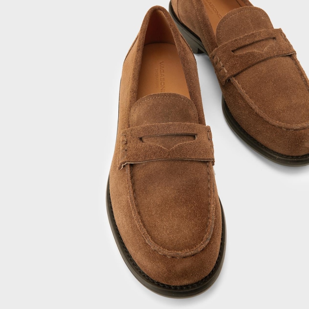 Brown suede loafers with a penny strap, rounded toes, and black soles photographed from above (pair shown).