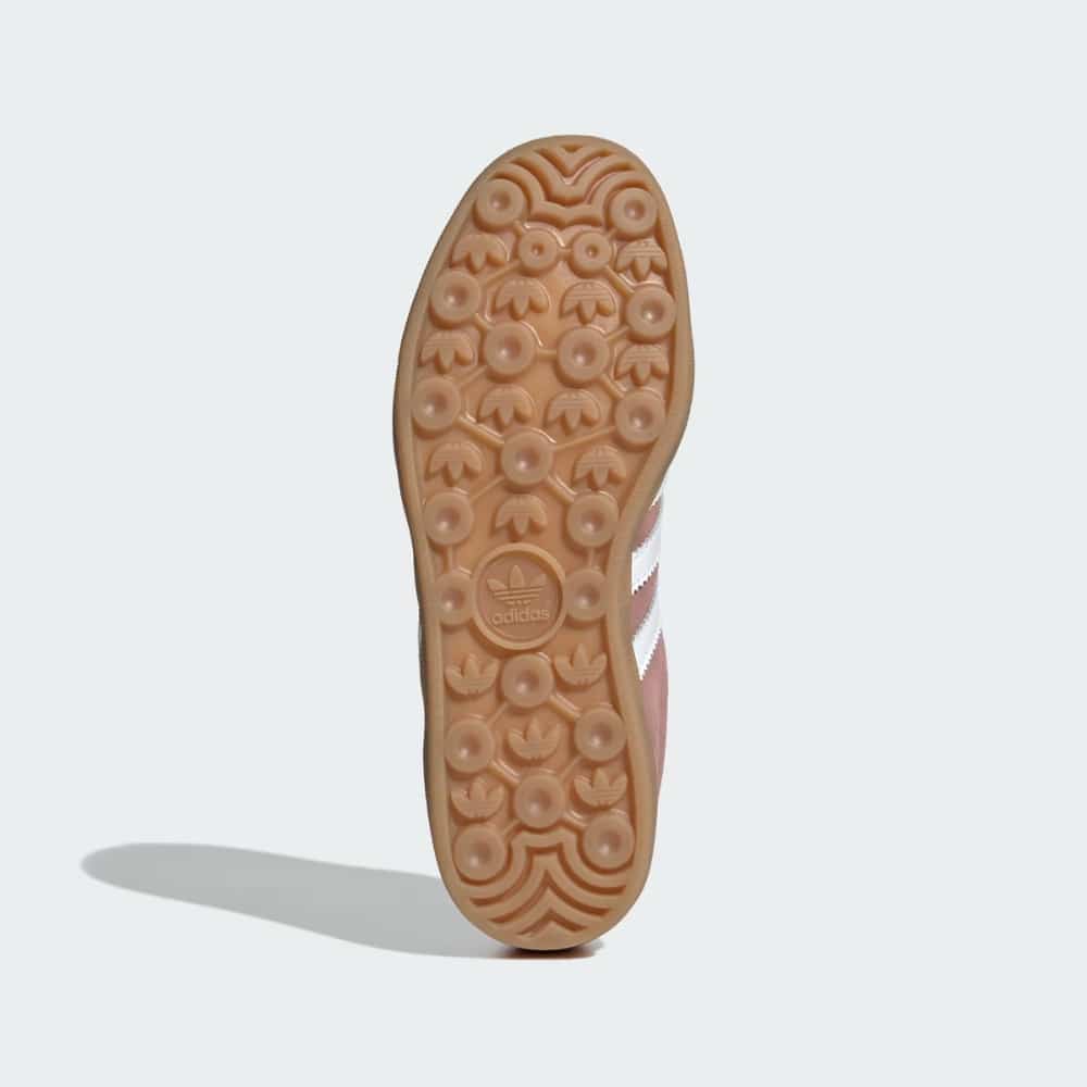 Bottom view of a gum-colored Adidas sneaker outsole with circular traction studs and central Adidas logo