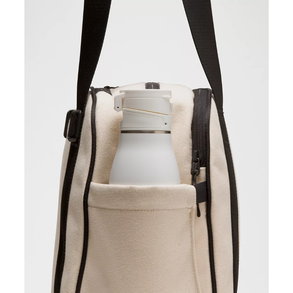 Beige canvas backpack with a light gray water bottle tucked into the front pocket of the bag as a carry setup.
