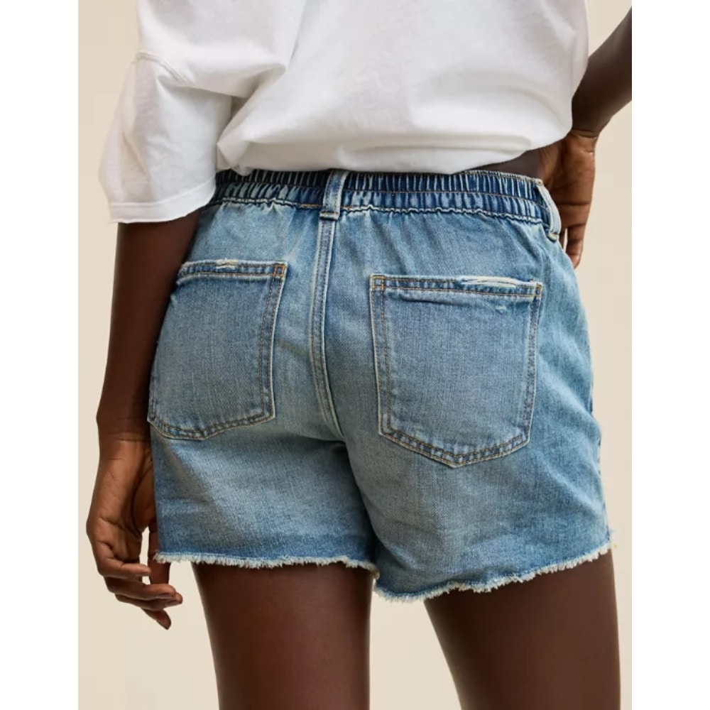 Person seen from behind wearing light-blue denim shorts with frayed hem and two back pockets, white shirt tucked in.