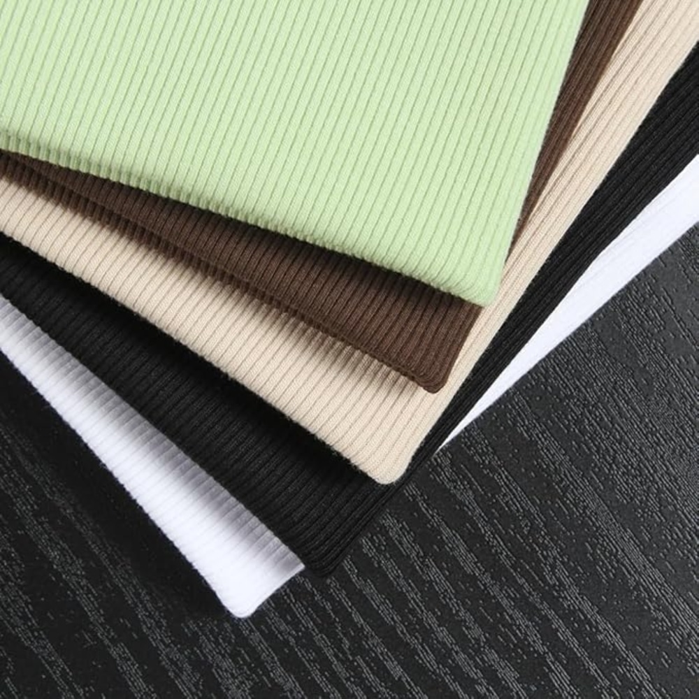 Stacked ribbed fabric swatches in green, beige, brown, cream, black, and white displayed on a dark textured surface.