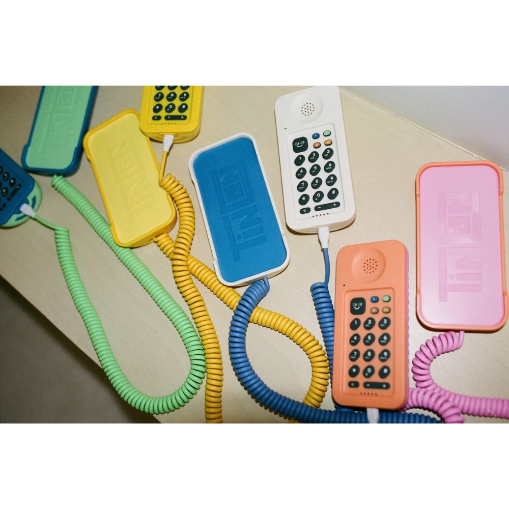 Several colorful corded landline phones with coiled cords on a light surface.