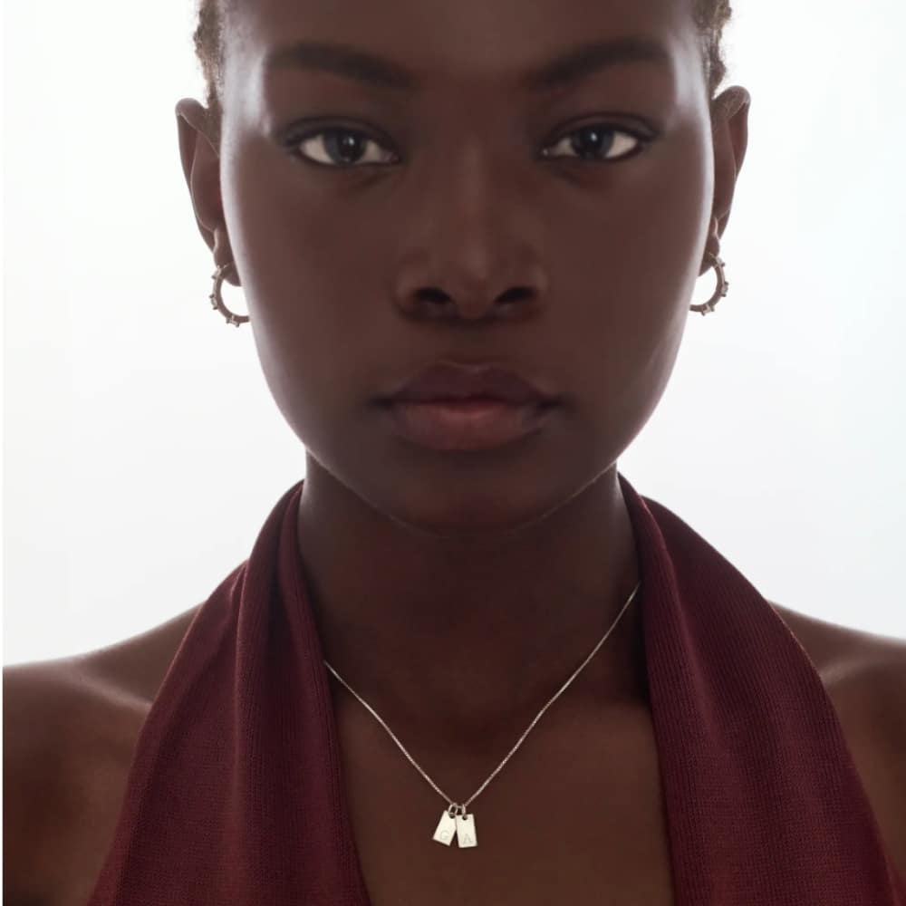 Close-up of a young woman with short hair, wearing a burgundy halter top and a silver necklace with two rectangular pendants.