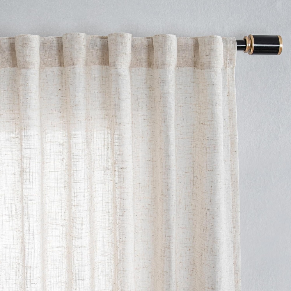 Cream linen curtain hanging from a black curtain rod with brass finial at right side.