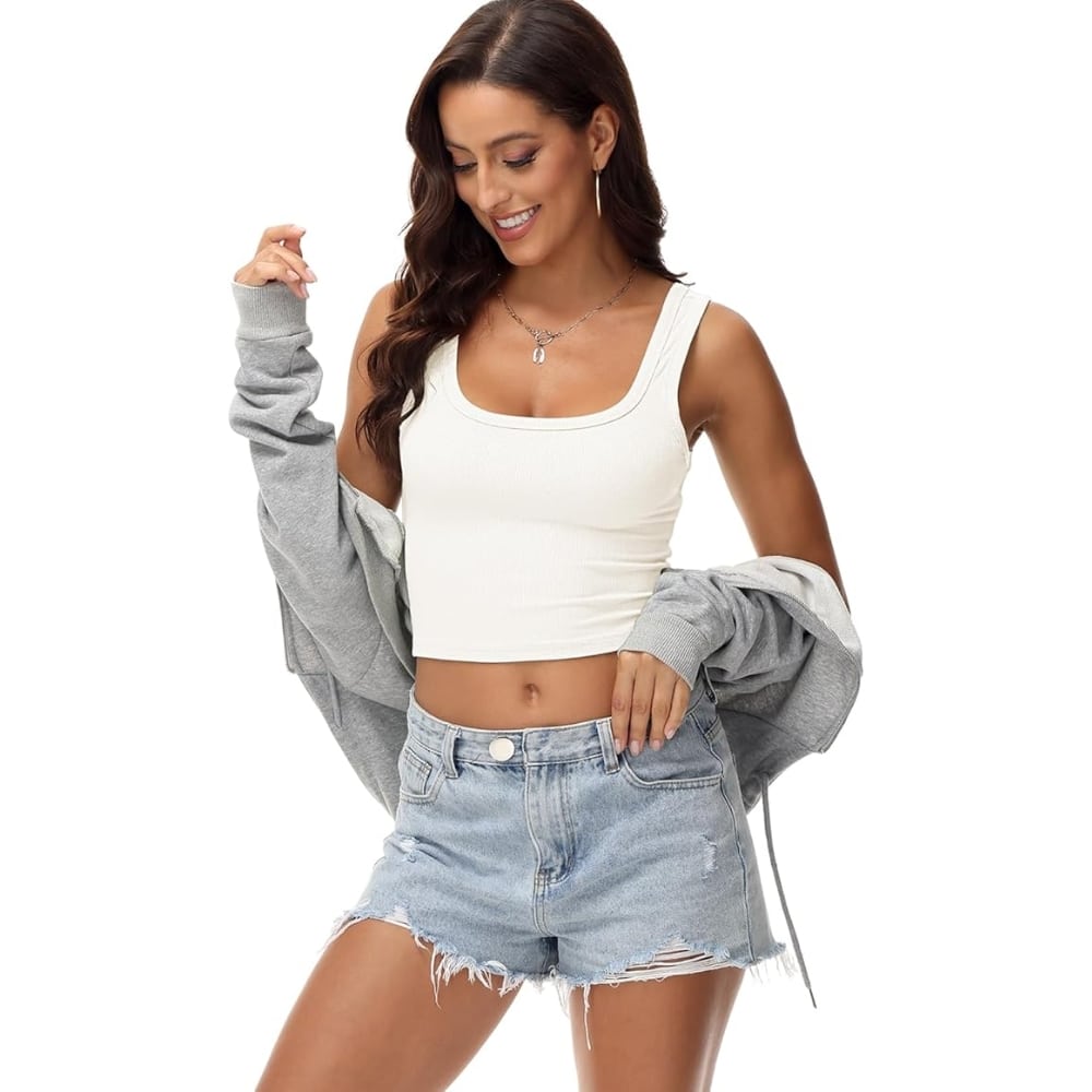 Woman modeling a casual summer outfit: white crop top and light denim shorts, with a gray jacket draped over her shoulders.