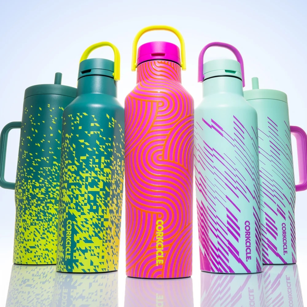 Four colorful Corkcicle water bottles with neon patterns lined up on a reflective surface, each with a distinct handle color.