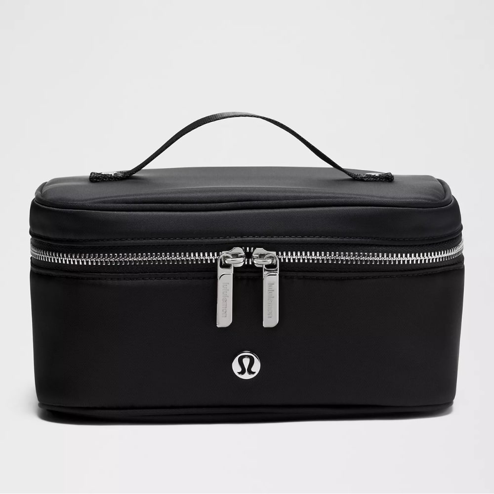 Black compact cosmetic bag with double silver zippers and a small top handle, featuring a silver logo badge on the front.