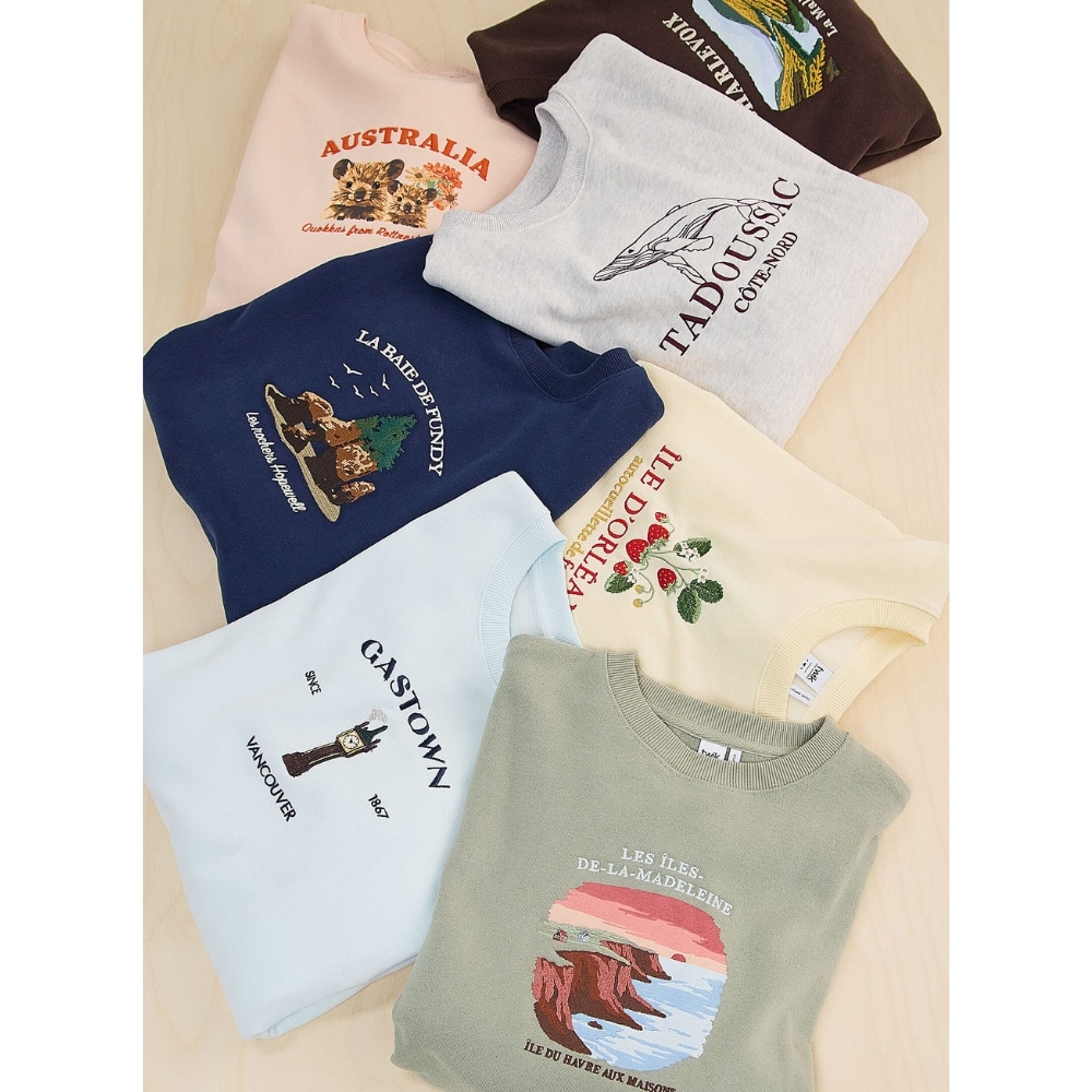 Six folded graphic T-shirts laid flat on a light wood surface, each with a different print and color.