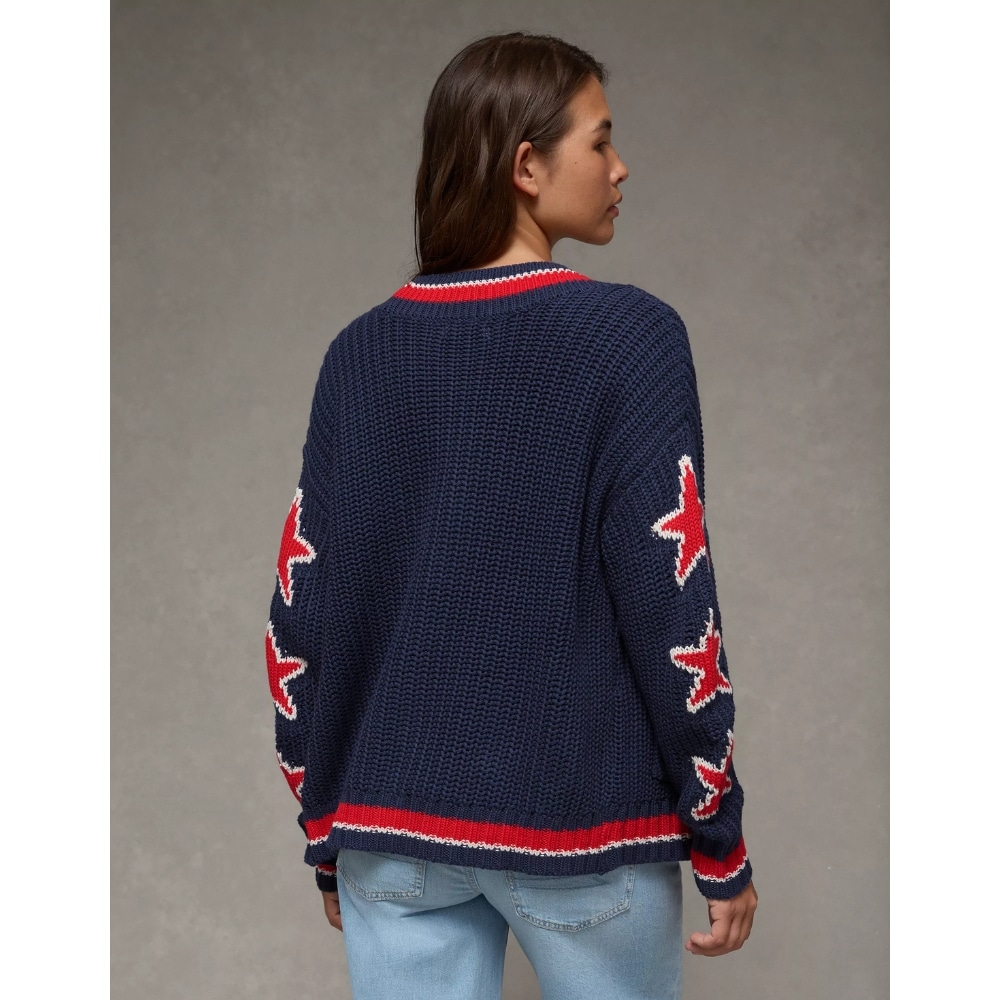 Back view of a person wearing a navy chunky knit sweater with red star patches along the sleeves and red-white striped hem and collar.