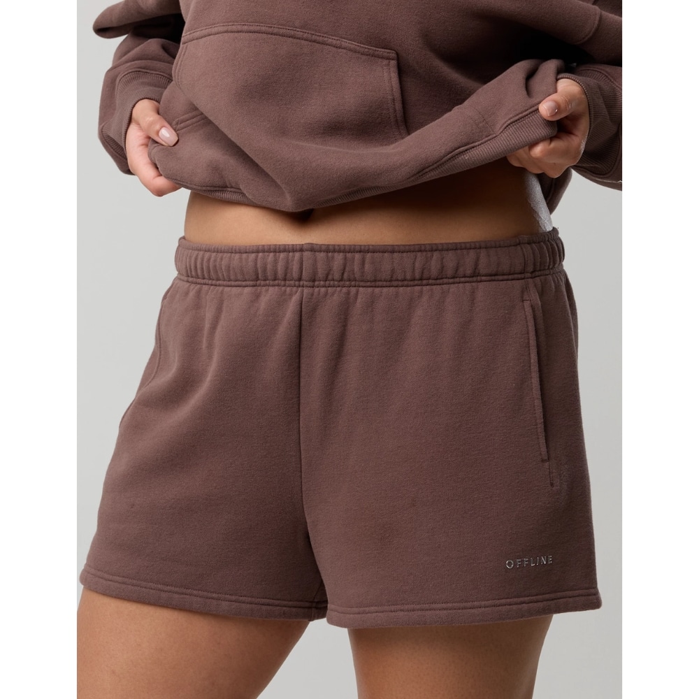 Brown jogger shorts with an elastic waistband, side pocket, and a small OFFLINE logo on the leg. A person lifts a brown hoodie, showing the midriff.