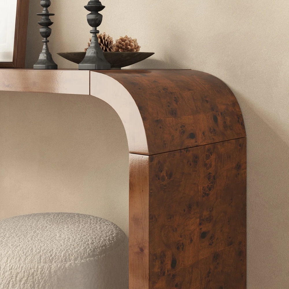 Wooden console with a curved corner and burl finish; on top are two black candle holders, a shallow bowl, and pinecones.