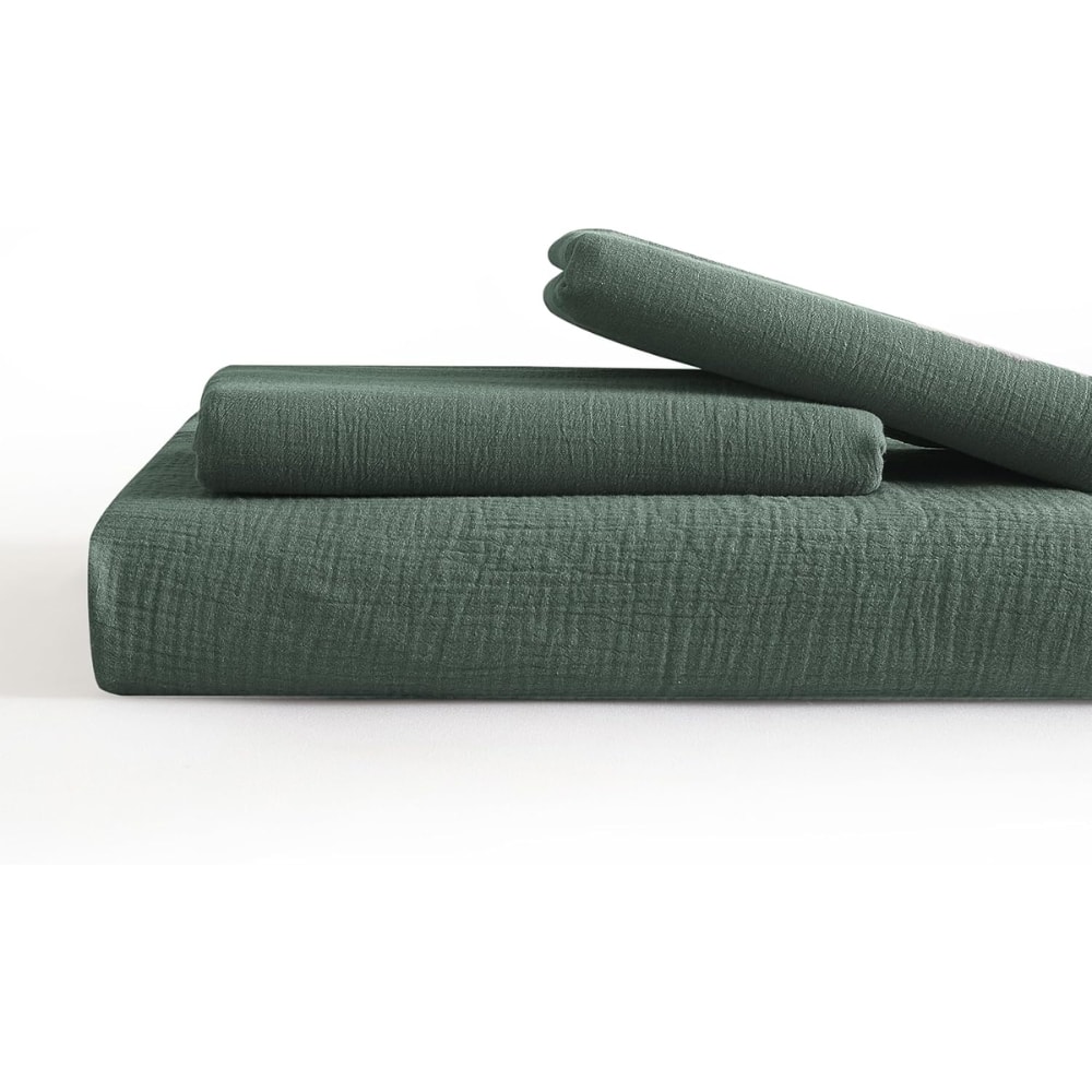 Stack of dark green fabric cushions arranged on a matching platform or mattress base. Two rolled cushions rest on top of a flat cushion, all in deep green fabric.