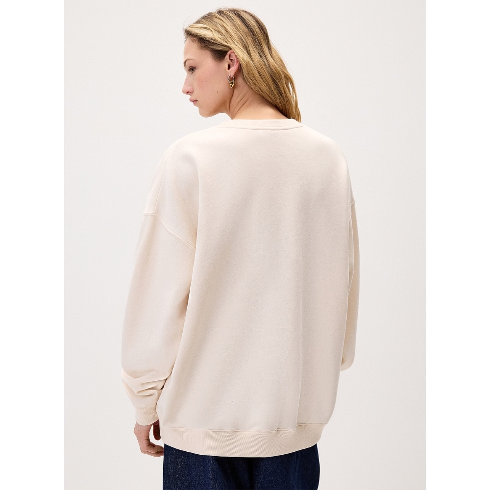 Back view of a person wearing a loose cream-colored sweatshirt with ribbed hem and cuffs, paired with dark jeans.