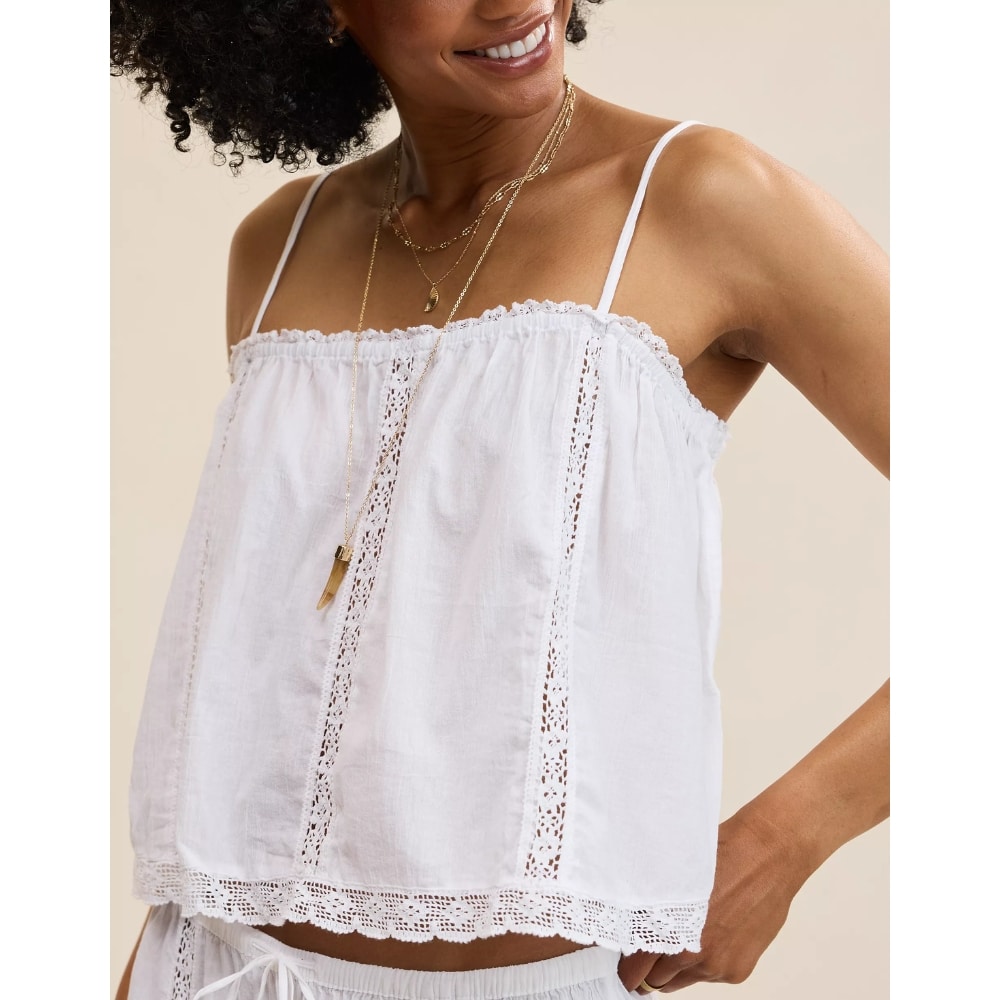 Woman in a white off-the-shoulder lace-trim top with thin straps and layered gold necklaces.