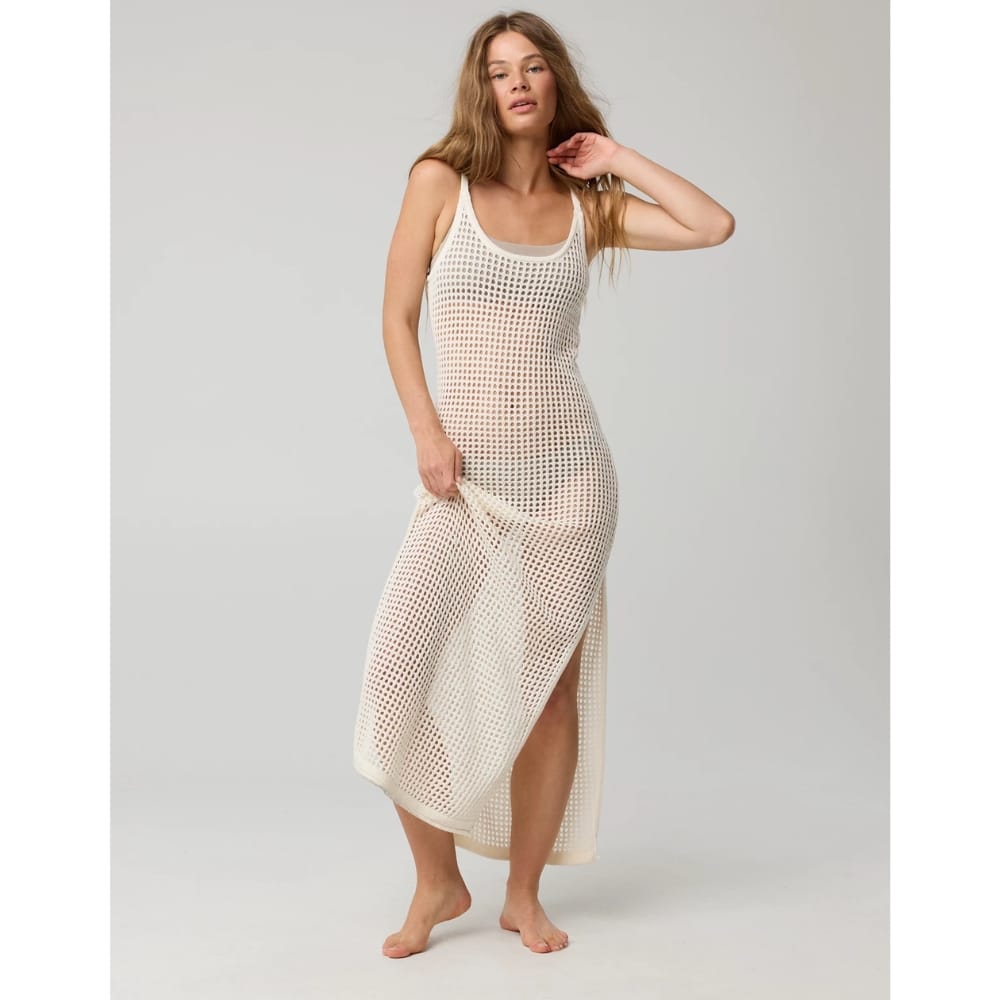Model wearing a sleeveless cream crochet mesh maxi dress, standing barefoot against a neutral backdrop, lifting the hem slightly.
