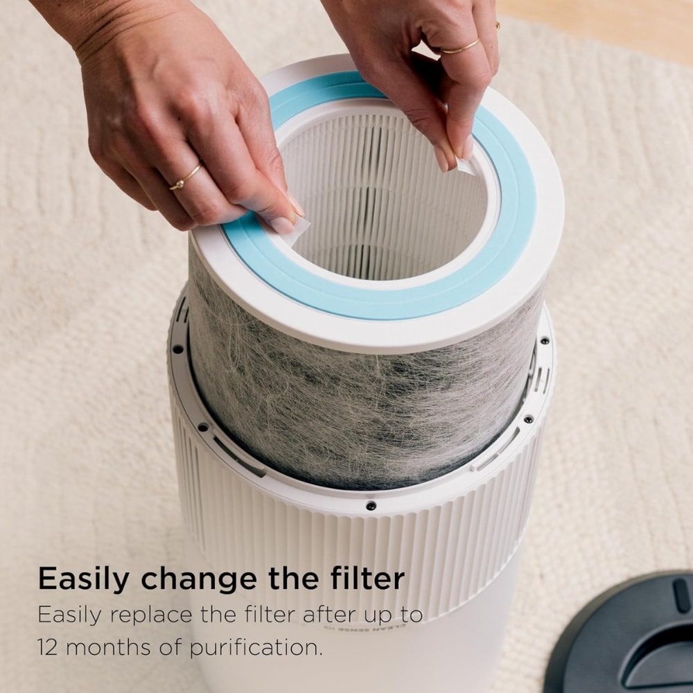 Hands inserting a new filter into a white cylindrical air purifier. It shows the filter being replaced by hand.
