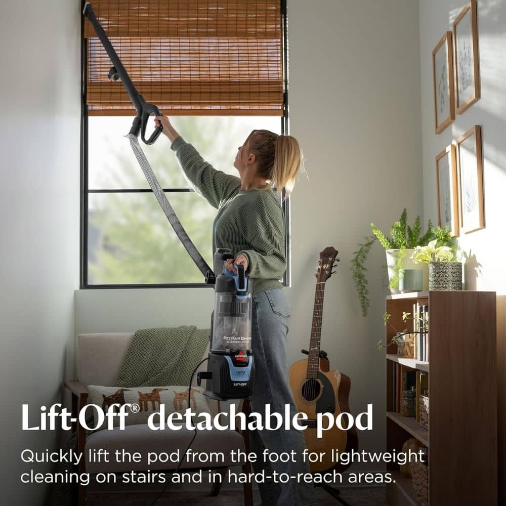 Person using a Lift-Off detachable pod vacuum to clean high window blinds in a living room.