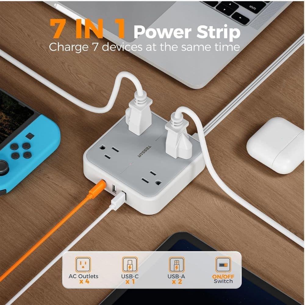 White 7‑in‑1 power strip on a wooden desk charging multiple devices at once, with AC outlets, USB‑C and USB‑A ports and an orange charging cable