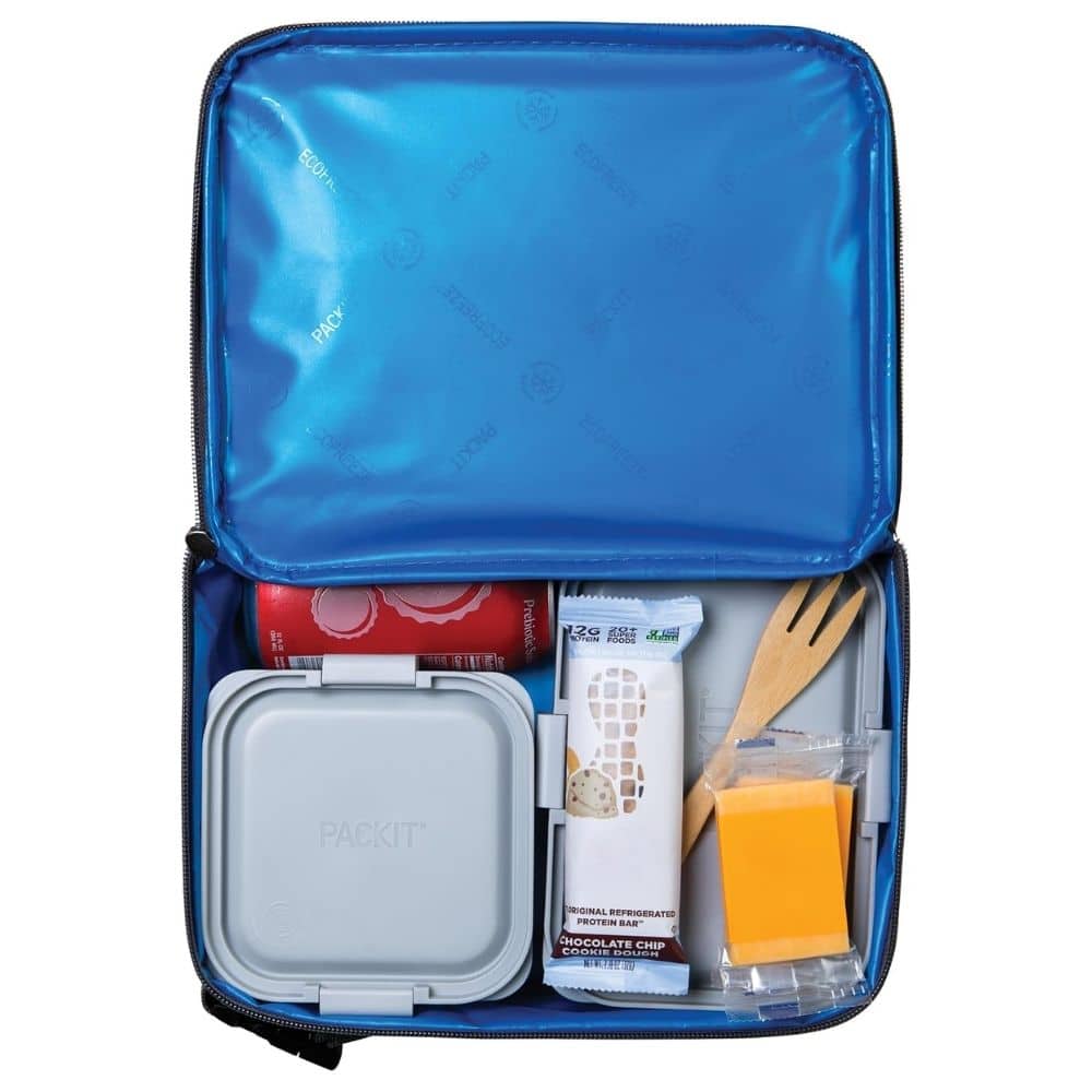 Open blue lunch bag revealing a gray square container, a protein bar, a wooden fork, and a small cheese block in a plastic bag.