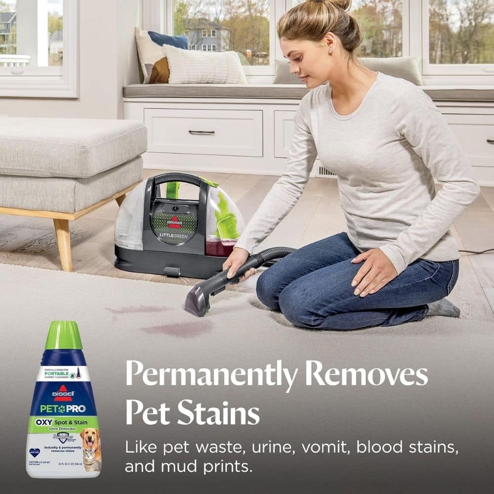 Woman kneeling on a light rug and using a carpet-cleaning machine to remove stains; a pet-stain remover bottle sits nearby in the foreground (advertisement).