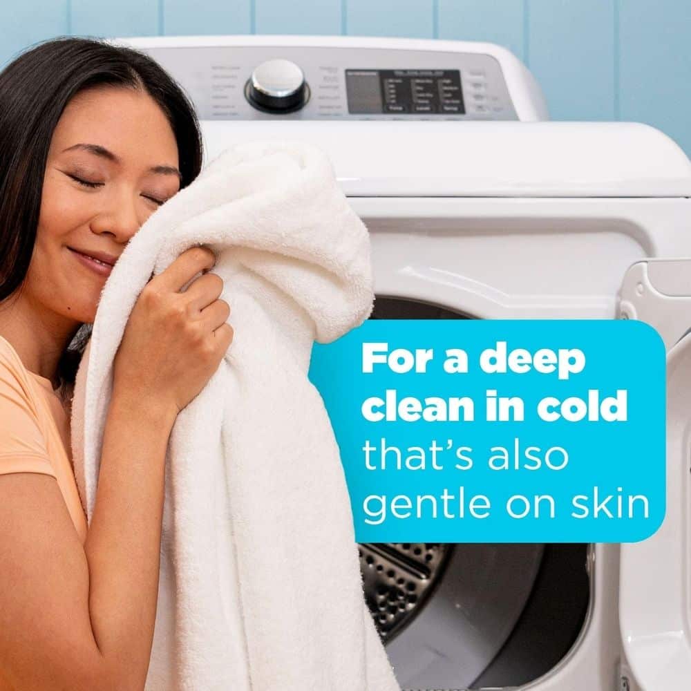 Woman holding a towel beside a washing machine, with a blue caption about a deep clean in cold that's gentle on skin.