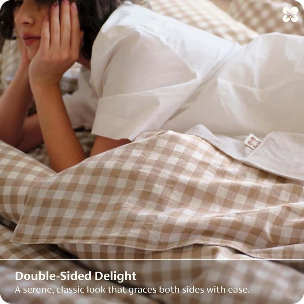 Person lying on a bed with a beige plaid comforter, resting their face in their hands as part of a bedding ad for Double-Sided Delight.