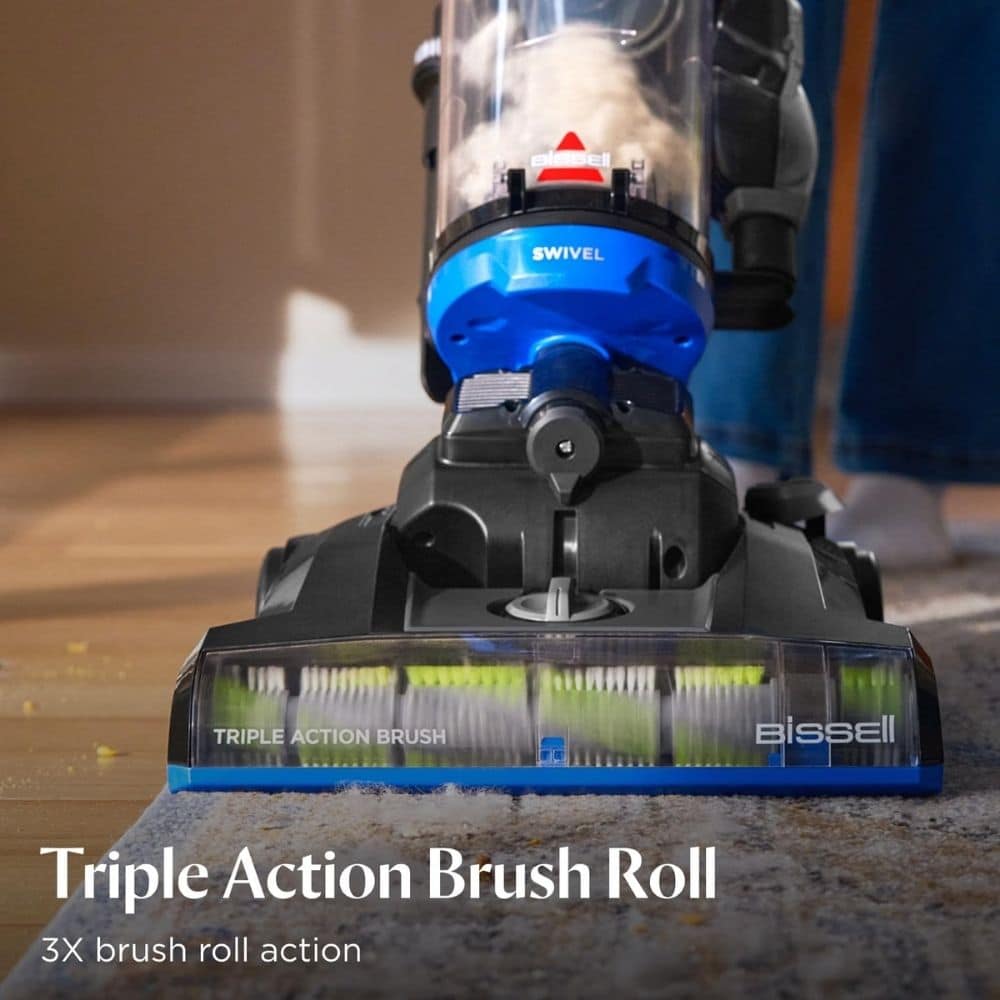 Bissell vacuum cleaner head with a blue Triple Action Brush Roll spinning on a carpeted floor.
