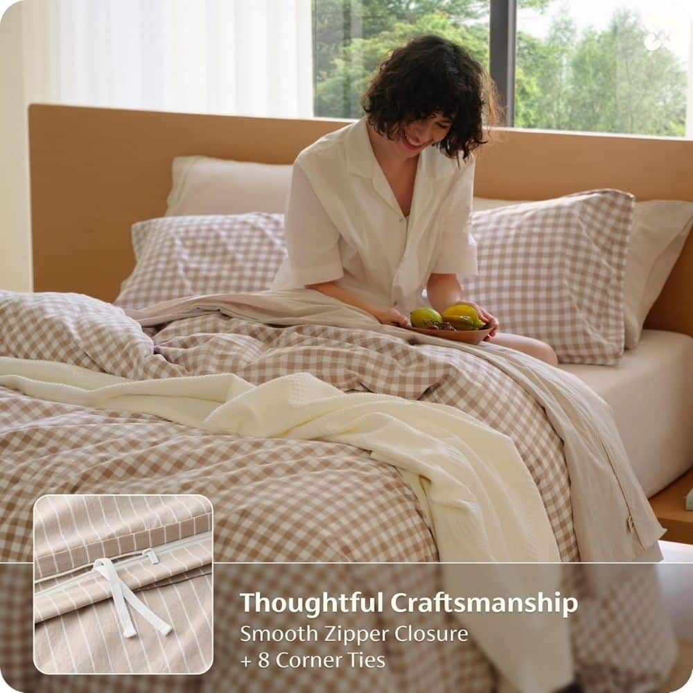 Woman sitting on a bed with beige plaid bedding, smiling while holding a plate of fruit.