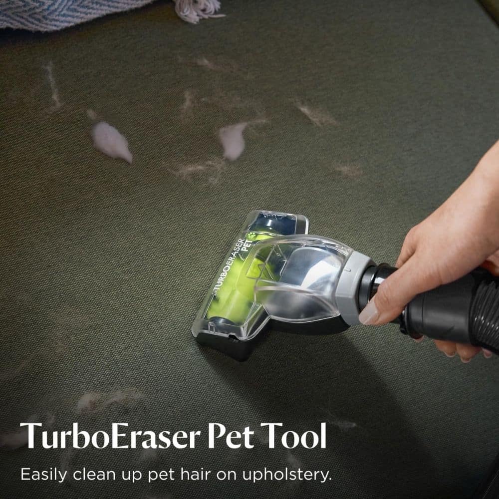 Hand holding a vacuum attachment scraping pet hair off dark upholstery, with product name TurboEraser Pet Tool visible and tagline 'Easily clean up pet hair on upholstery'