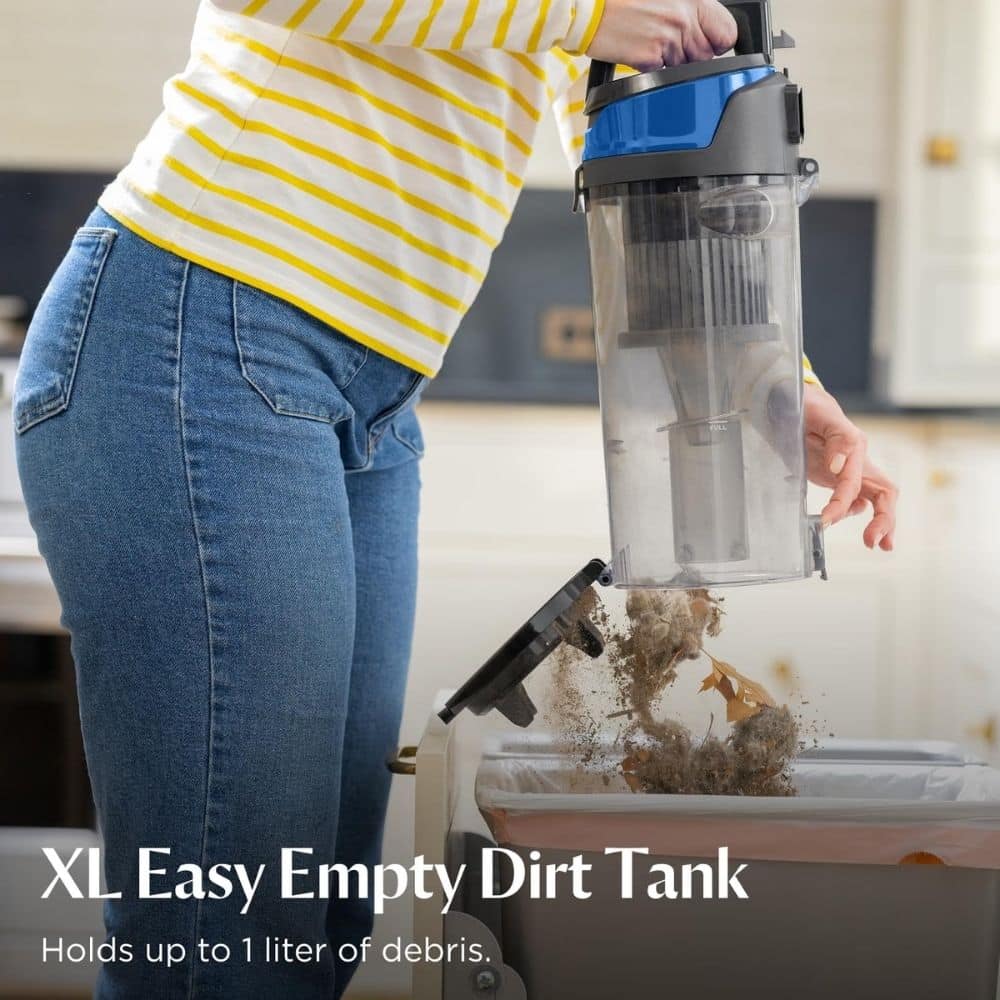 Person in a yellow-striped shirt empties a vacuum's dirt tank into a trash bin, debris spilling on the rim.