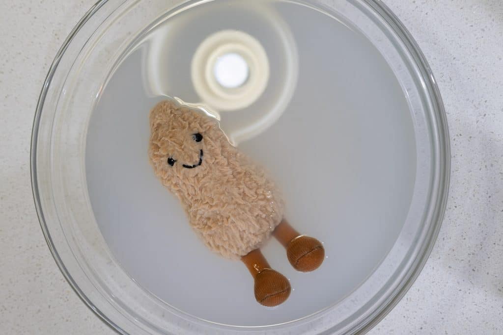 _K9A5268 - House Work Soft teddy bear toy submerged in a clear bowl of milky water on a kitchen counter