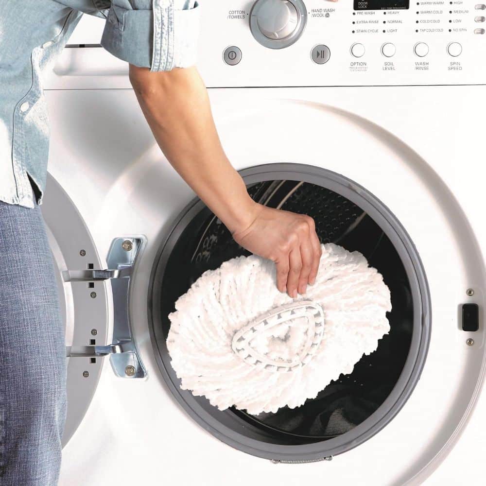 Person placing a large white fluffy laundry item into a front-loading washing machine door, preparing to wash it.