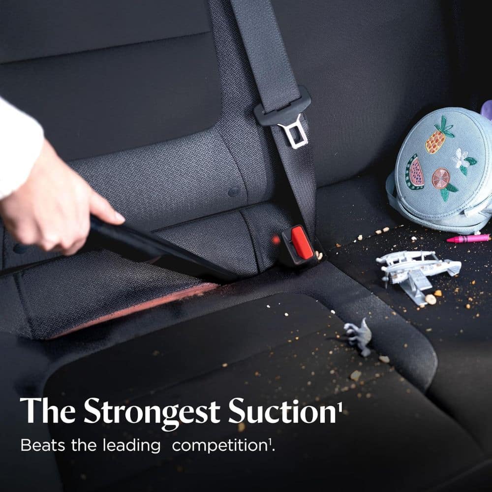 Person vacuuming a car seat, debris scattered on the seat with a backpack nearby; overlay text reads 'The Strongest Suction' in an advertisement.