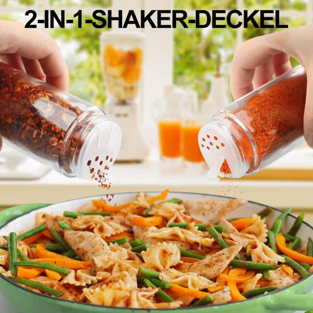Two hands tilt spice shakers labeled '2-in-1 Shaker-Deckel' to sprinkle red pepper flakes onto a pasta dish with chicken and vegetables.