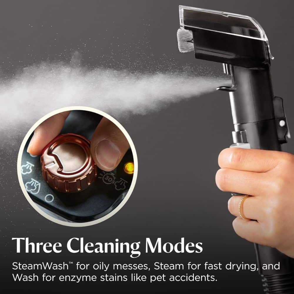 Hand-held cleaning device sprays a mist toward a circular control dial showing three modes: SteamWash, Steam, and Wash for stains and messes.